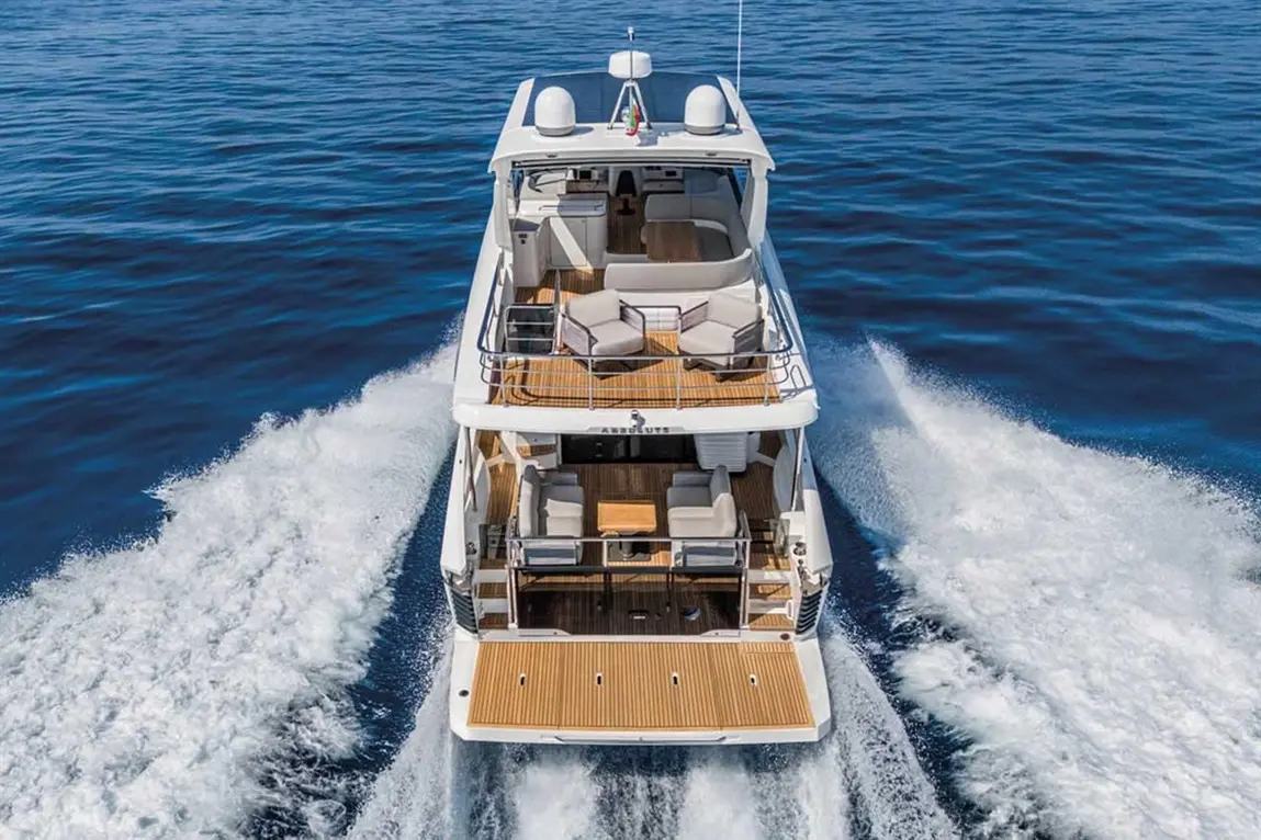 A luxury yacht with a spacious deck and seating, cruising through calm blue waters, leaving a wake behind.